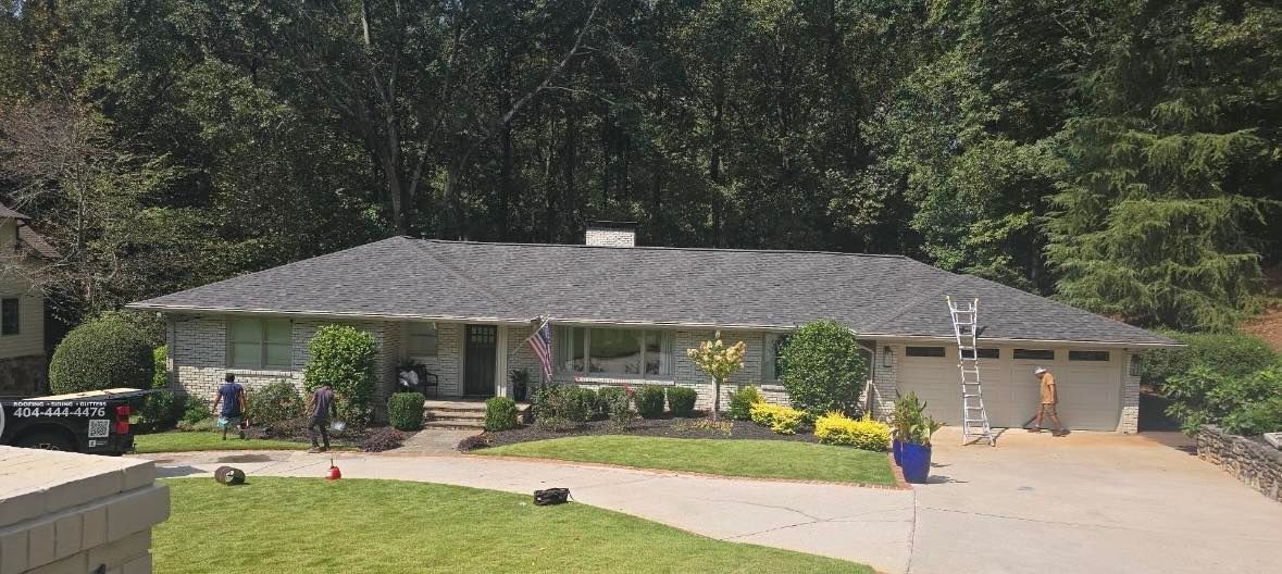 A gray-roofed house with a light-colored exterior, green lawn, and trees in the background.
