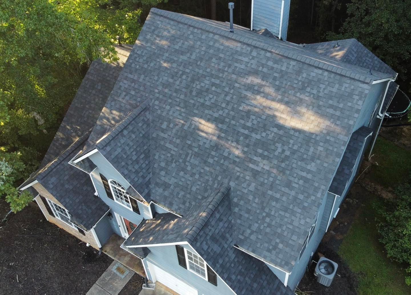 Aerial view of a blue house with a dark gray shingle roof and surrounding trees.