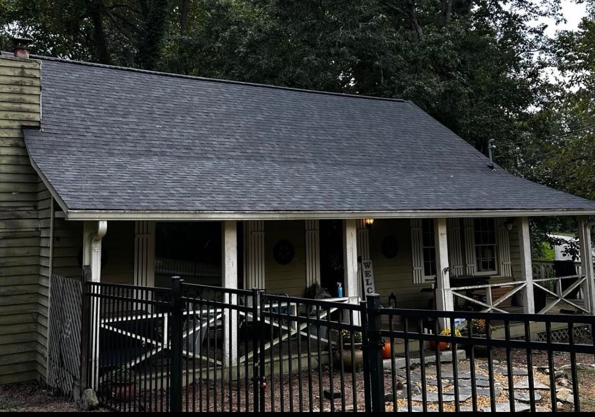 House with dark roof, porch, ramp, black fence, and trees in the background.