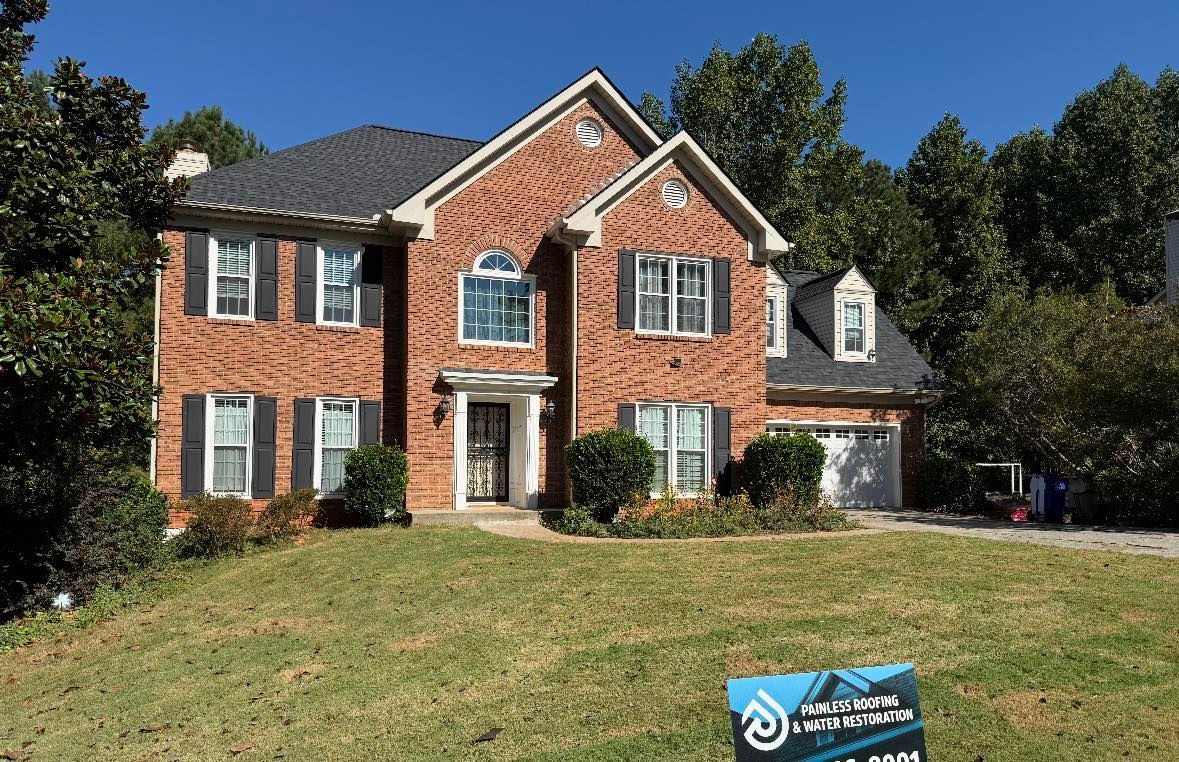 Two-story brick house with a dark gray roof on a sunny day. A sign is in the front yard.