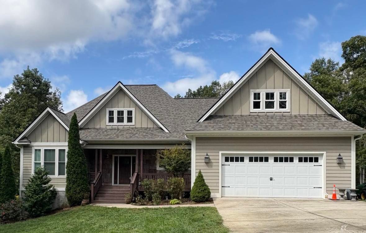 Beige house with a brown roof and white garage door against a partly cloudy sky.