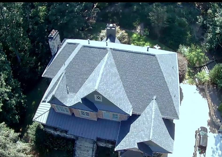 Aerial view of a gray roofed house, surrounded by trees and a driveway.