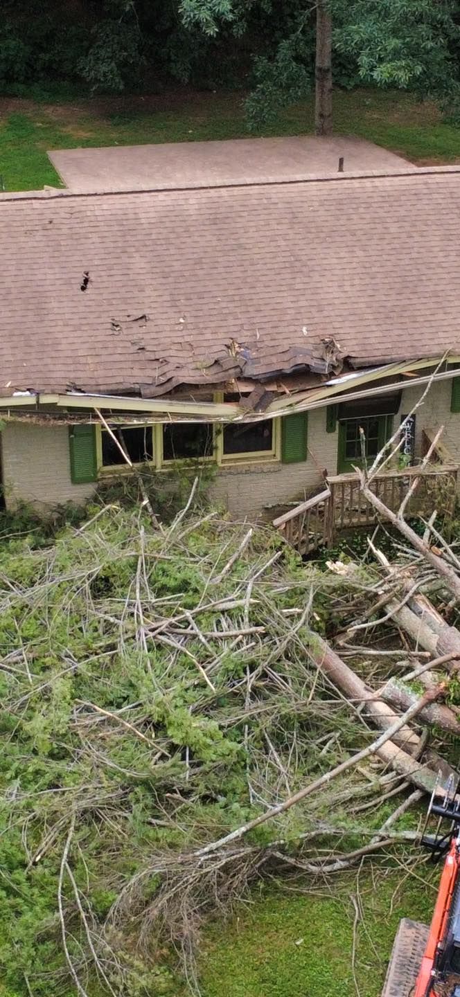 A house with a damaged roof and fallen branches and debris in front.