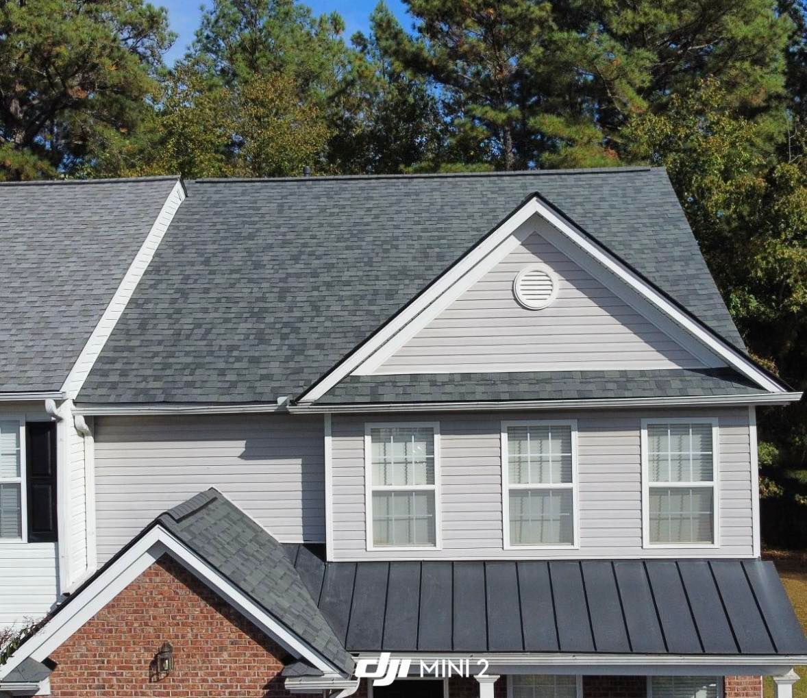 Gray house with shingle roof, white trim, and a brick section below. Windows are white.