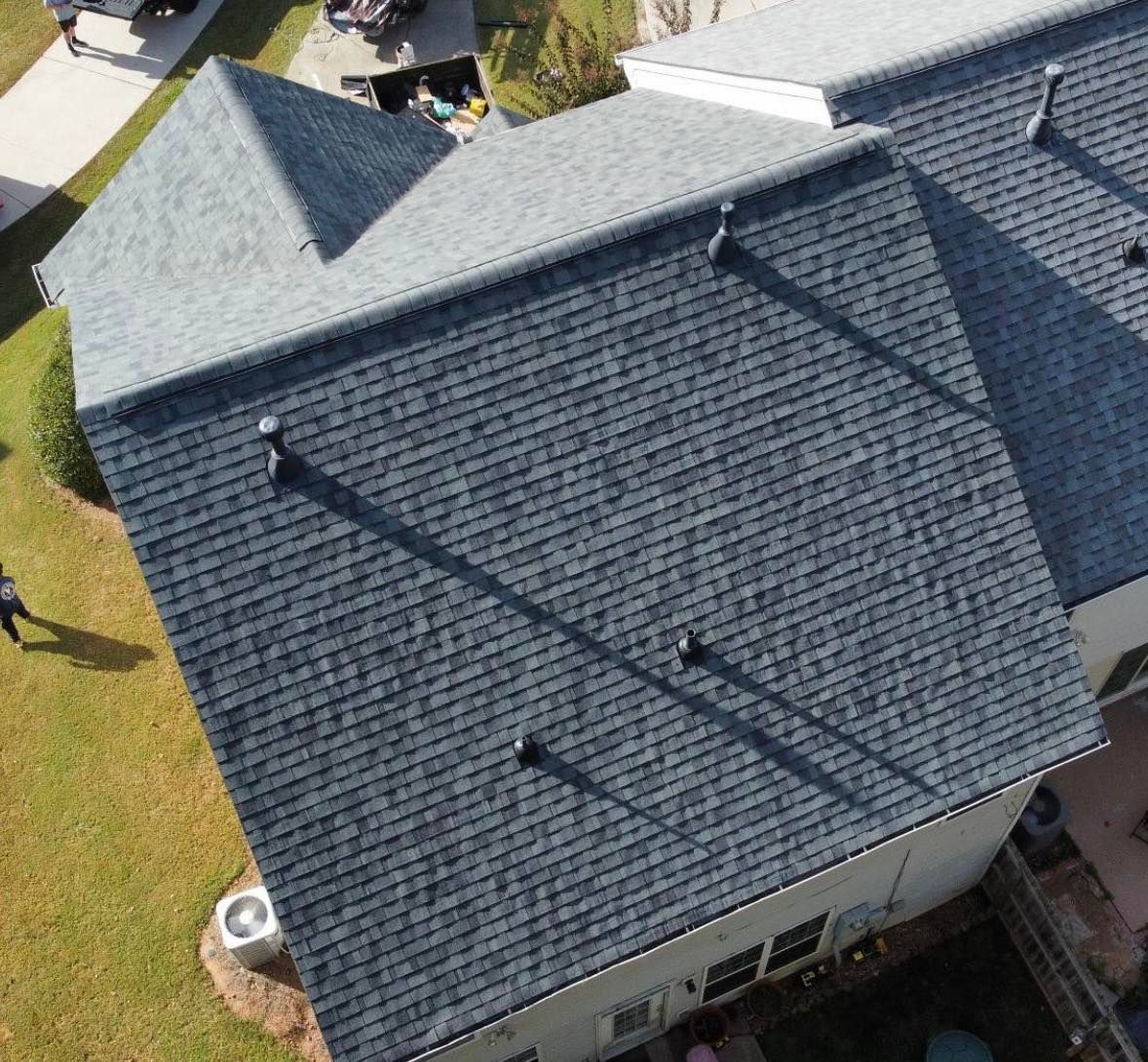 Aerial view of a gray shingle roof on a two-story house with dark vents casting shadows on the roof.