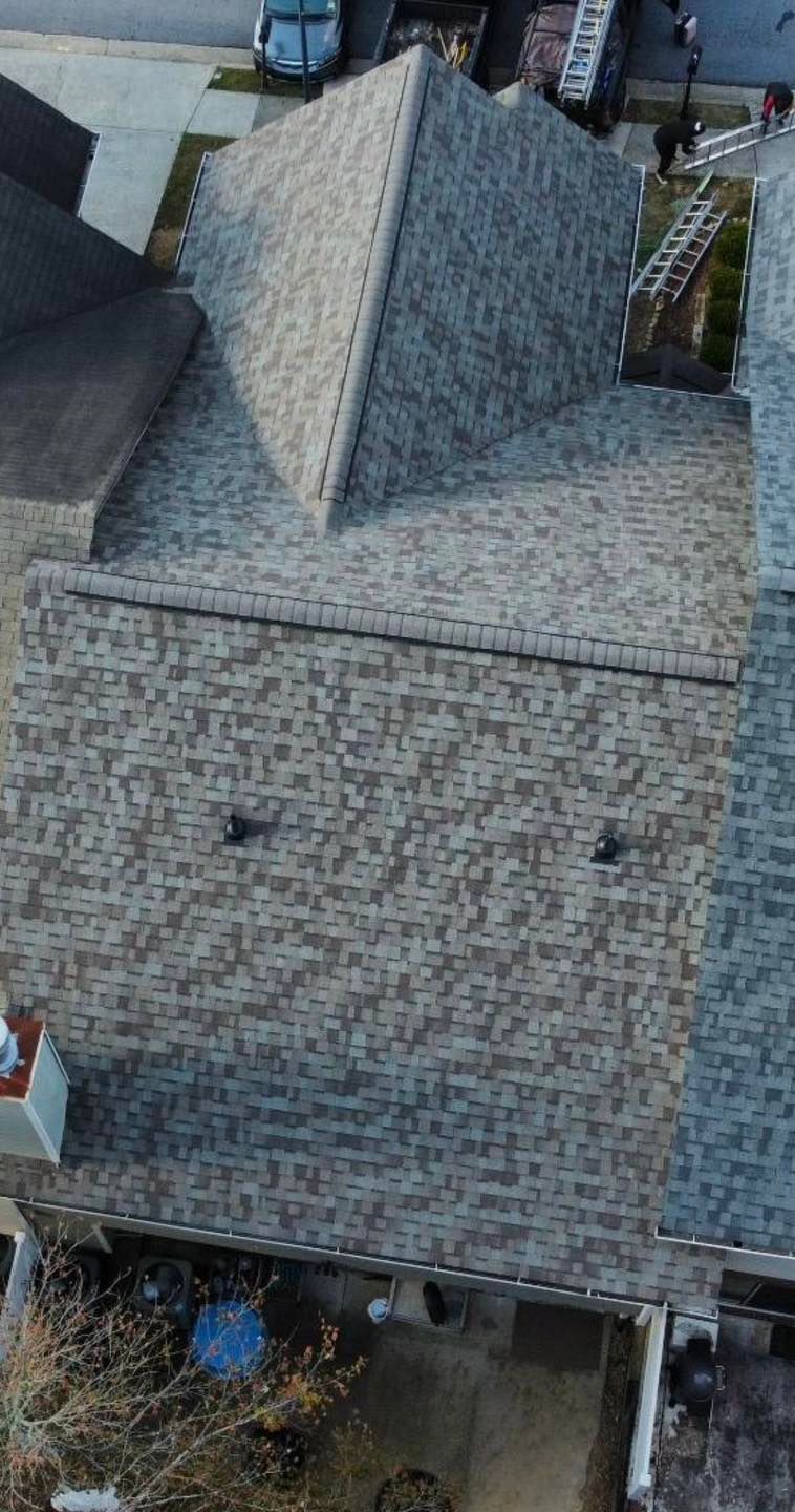 Overhead view of a house with gray, patterned shingles; a white van and tools are in the background.