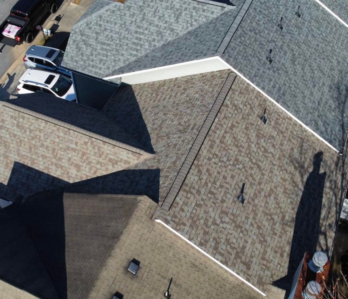 Aerial view of multiple gray and brown shingled roofs with a shadow cast across the surface.