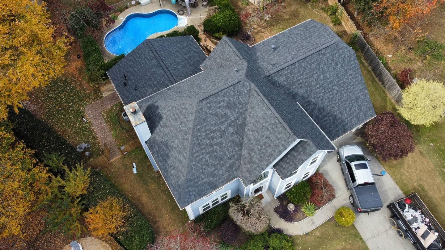 Aerial view of a gray-roofed house with a blue pool, surrounded by autumn trees and a driveway with a truck.