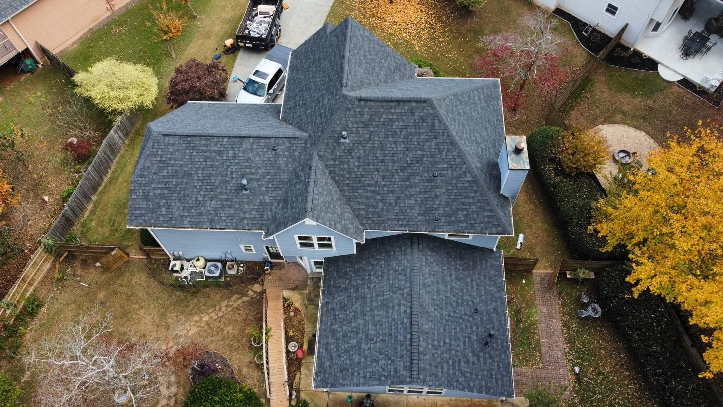 Overhead view of a house with a dark gray shingled roof, autumn foliage, and a truck parked nearby.