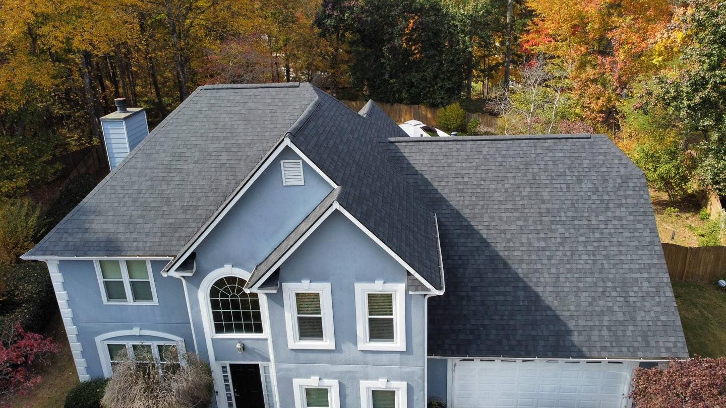 Blue house with gray roof, surrounded by trees with fall foliage.