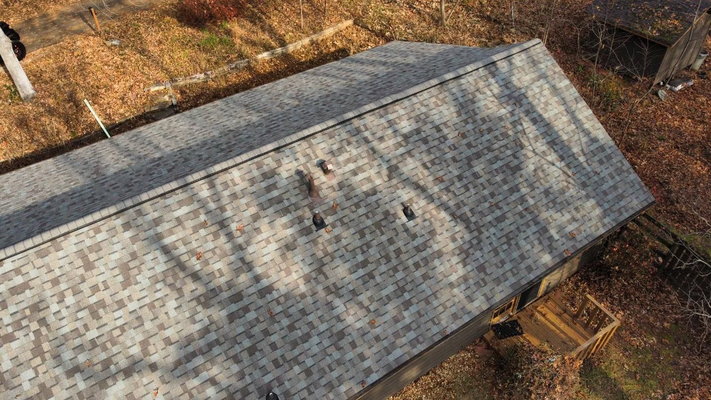 Overhead view of a gray shingle roof with three visible vents, set among bare trees and autumn foliage.