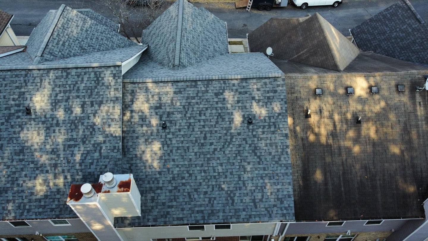 Overhead view of several dark gray shingled roofs with chimneys, casting long shadows.
