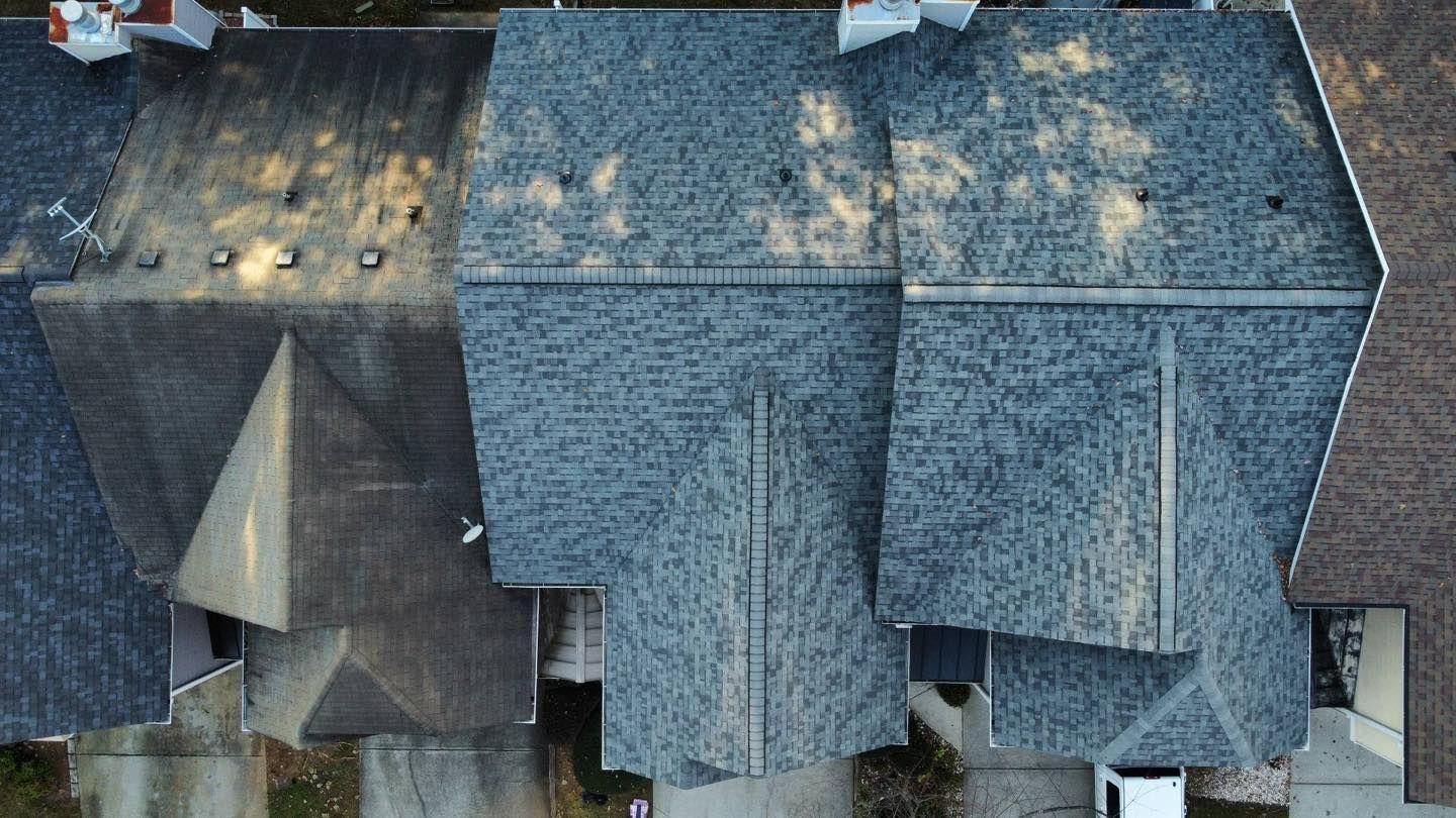 Overhead view of gray shingled roofs of attached houses, sunlight casts shadows.