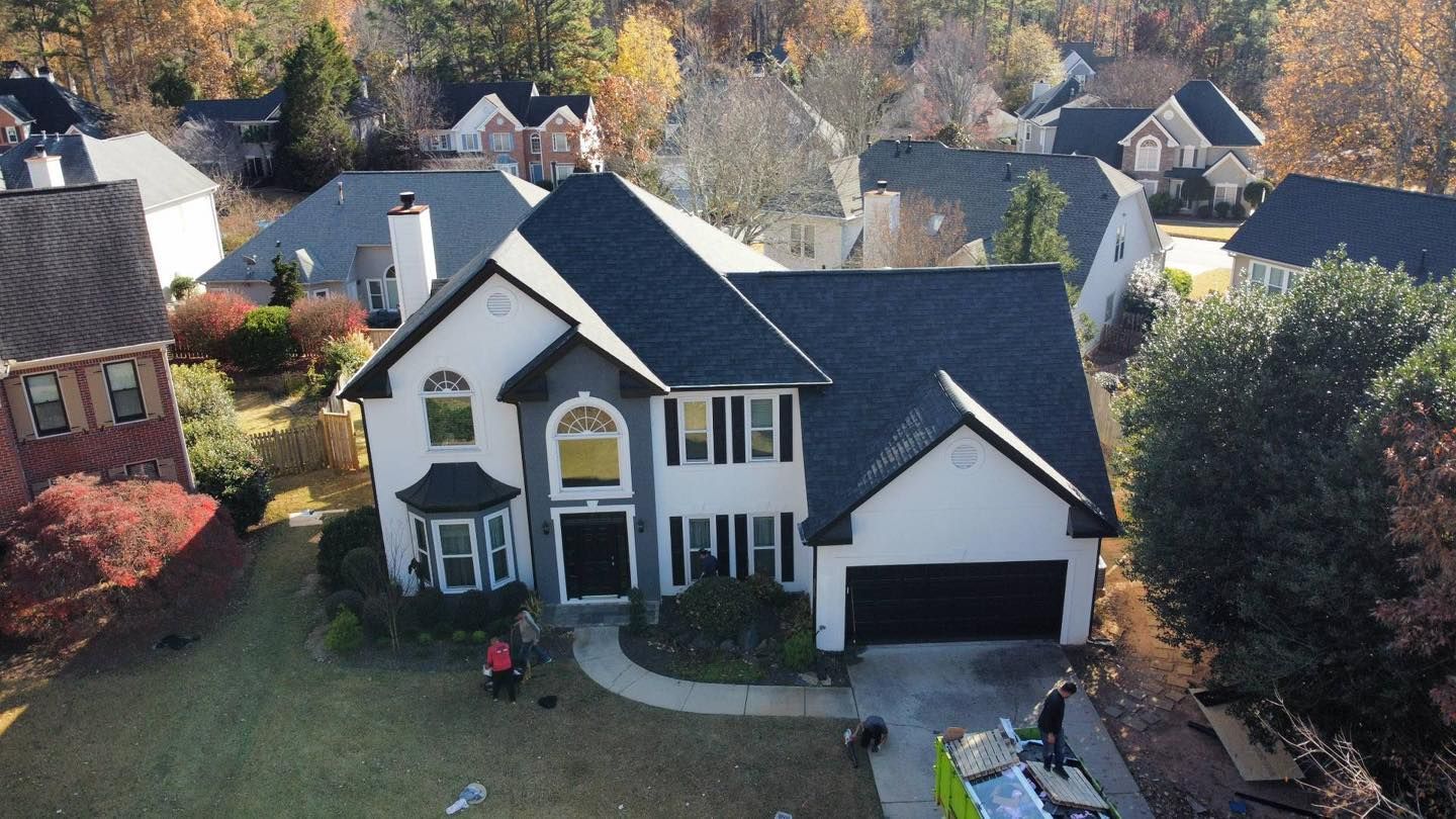 Two-story house with dark roof and garage, surrounded by other houses and trees in autumn.