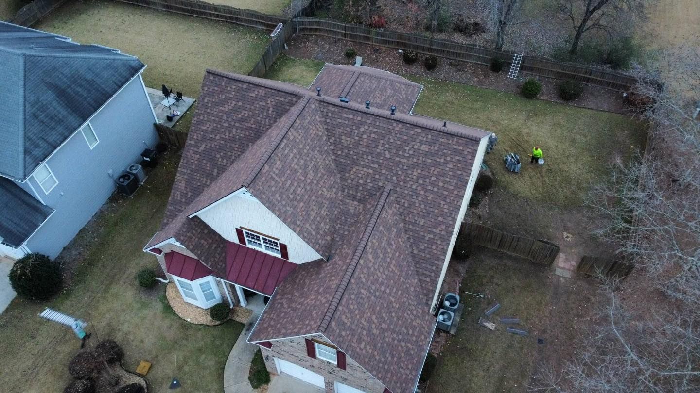 Overhead view of a house with a brown roof and a small yard. Two people are working in the yard.