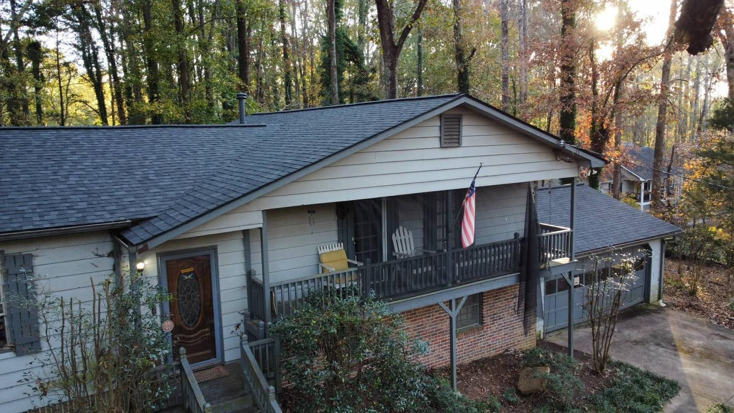 Cottage with a dark roof and porch, American flag, surrounded by trees.