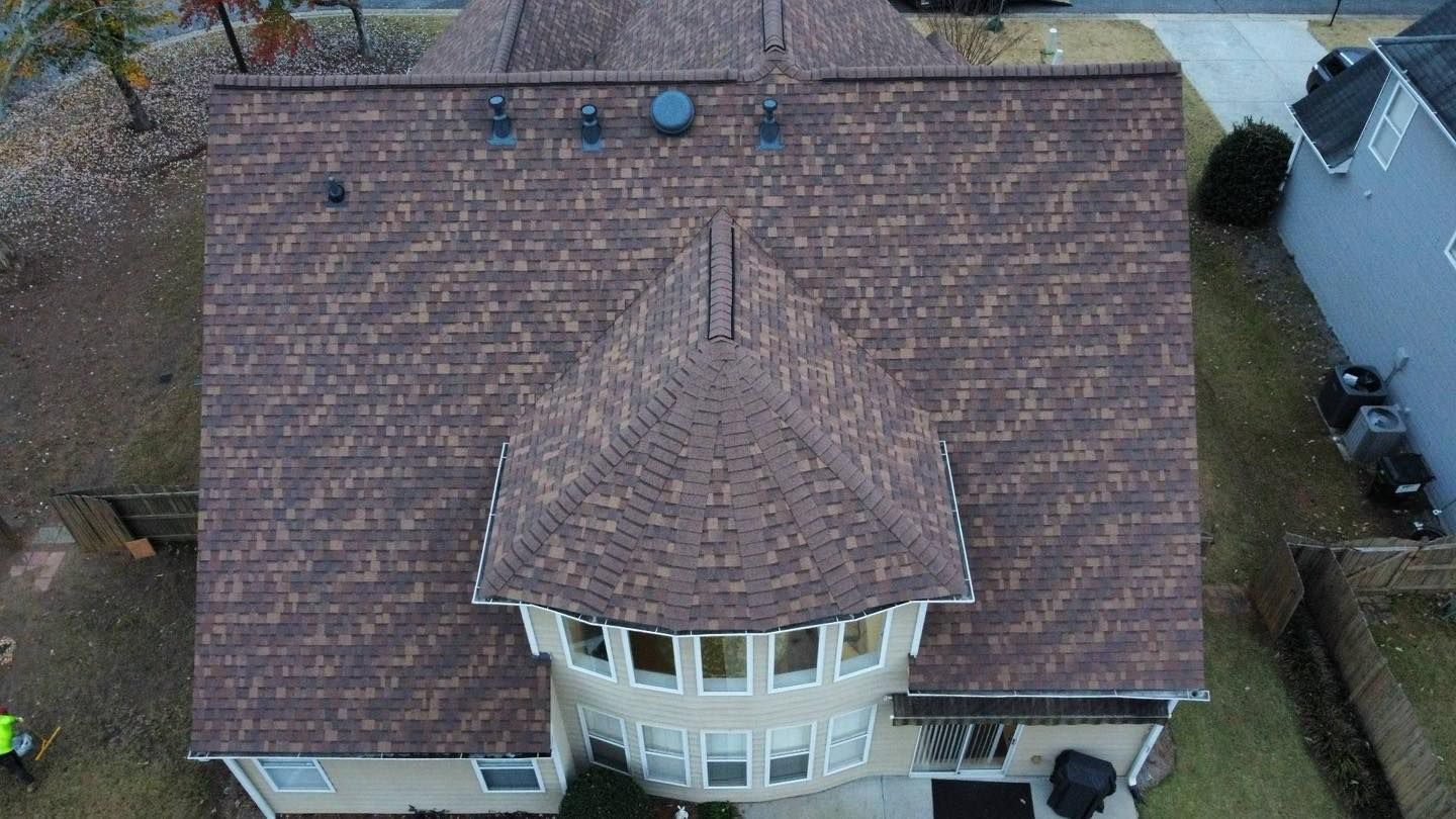 Overhead view of a house with a brown shingle roof, surrounded by lawn and some trees.