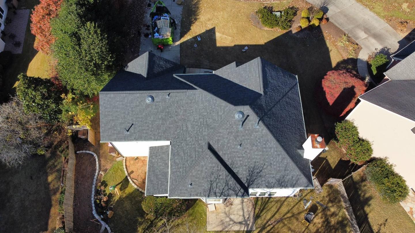 Overhead view of a house with a dark gray roof surrounded by trees and a driveway.