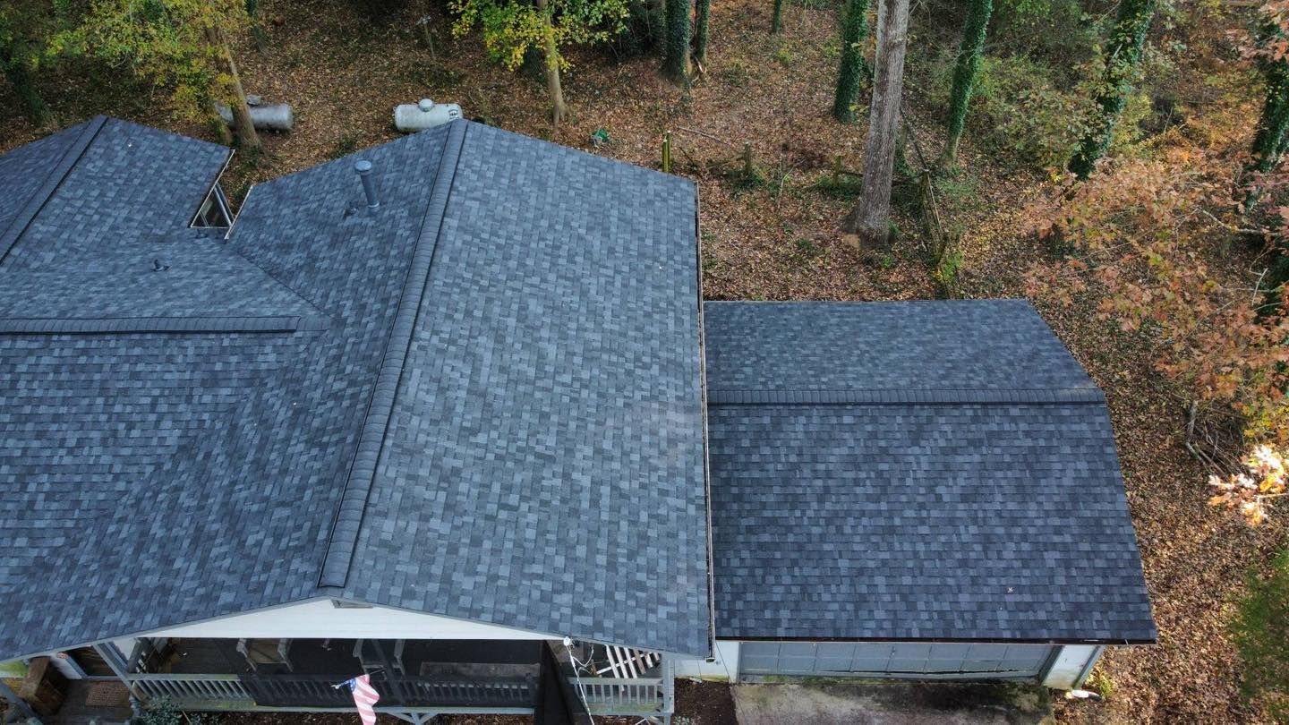 Overhead view of a house with a dark gray shingle roof, surrounded by trees.