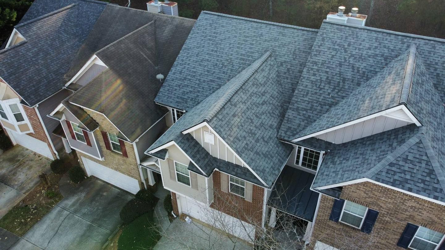 Row of townhouses with gray shingle roofs, various brick and siding colors, and garage doors.