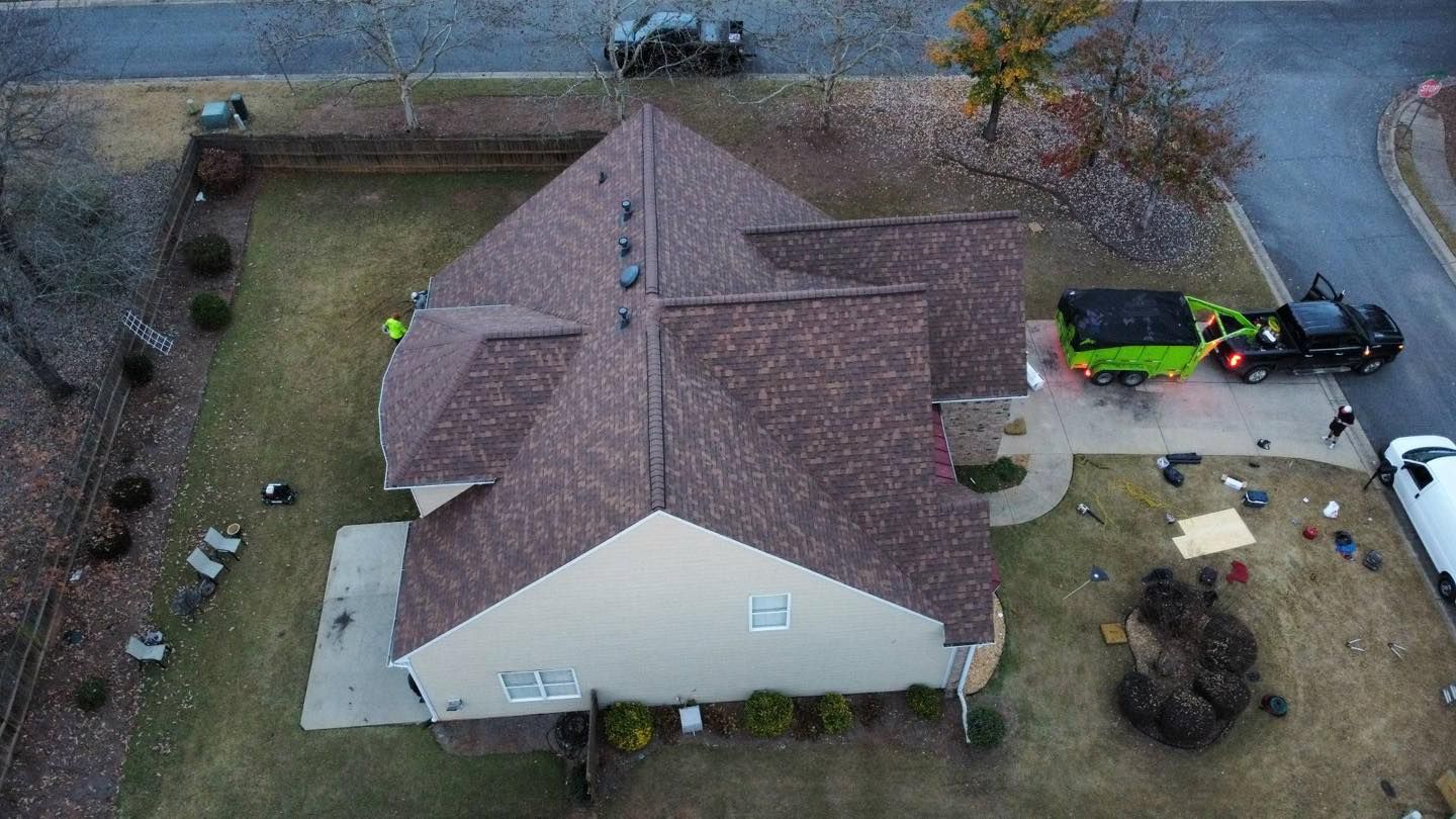 Overhead view of a house with roofing crew working; trucks, materials and trees are also present.