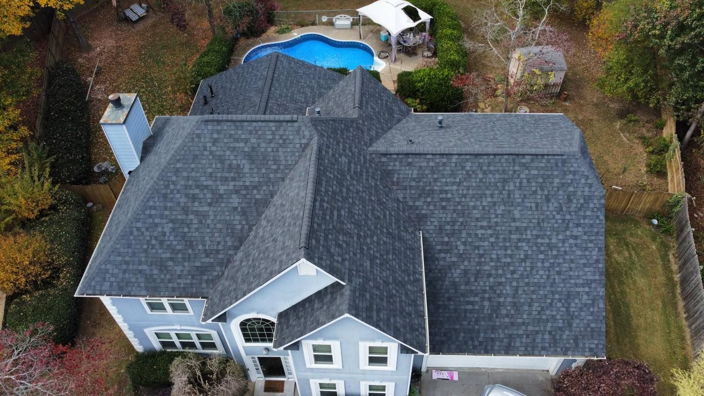 Aerial view of a gray house with a dark gray roof, a pool, and surrounding fall foliage.