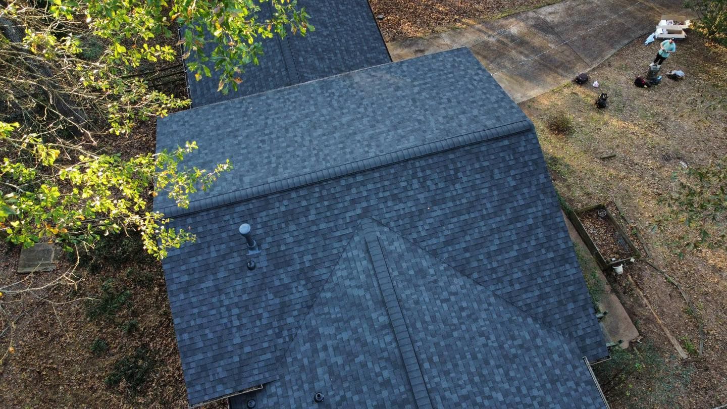 Dark gray shingle roof of a house with trees on the side; aerial view.