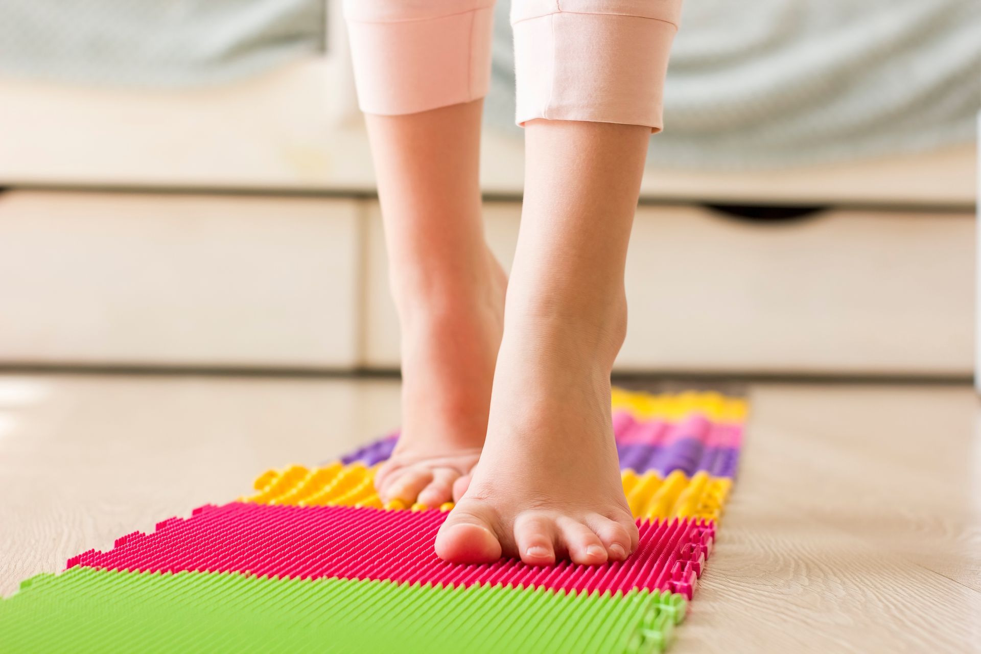 Bare feet walking on a colorful textured mat indoors.