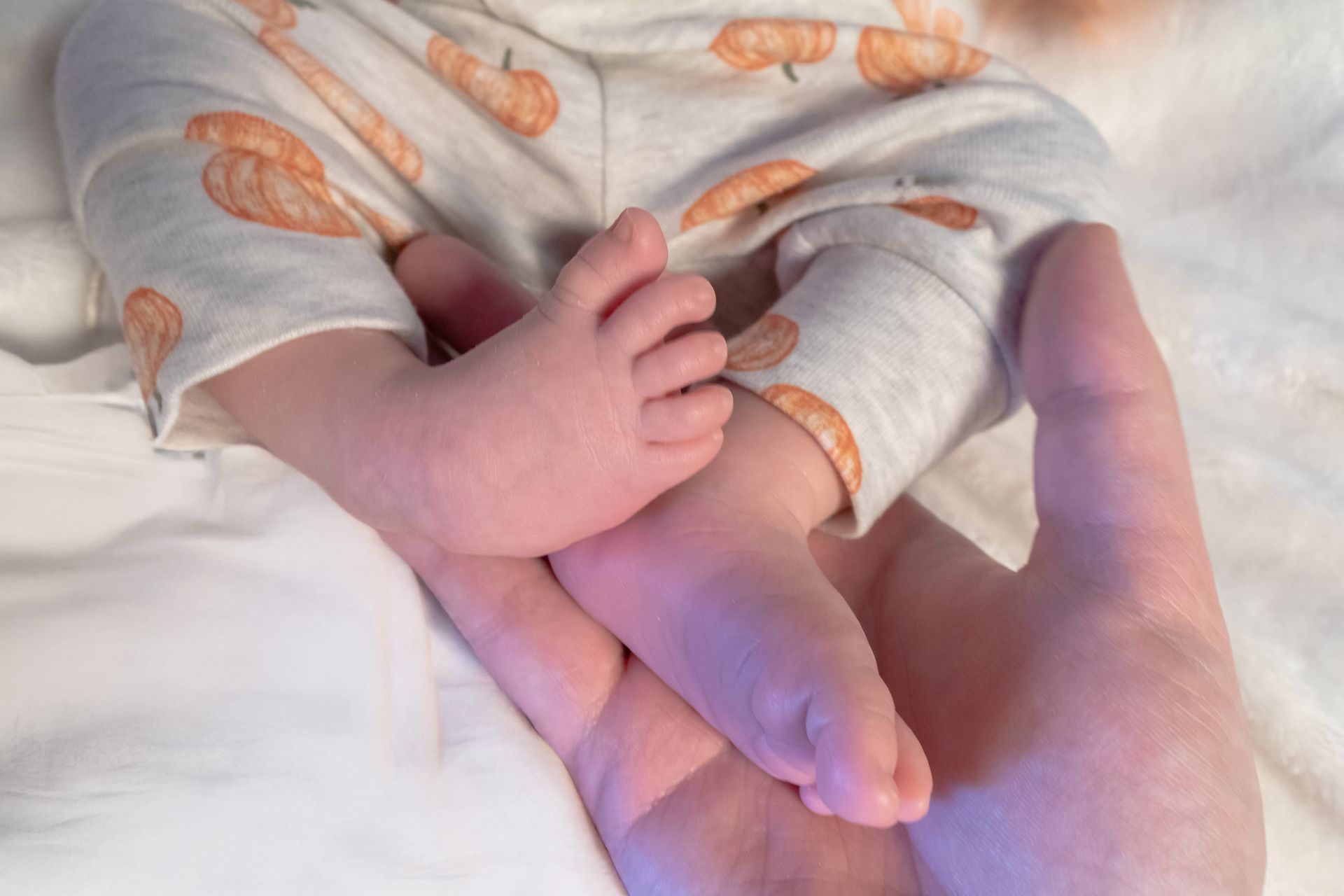 Baby feet resting in a large hand, wearing pumpkin-patterned pajamas.