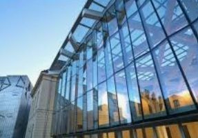 Modern glass office building reflecting city skyline at sunset