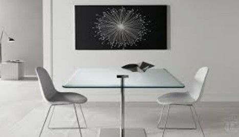 Minimalist white dining room with a glass table, two chairs, and black abstract wall art.