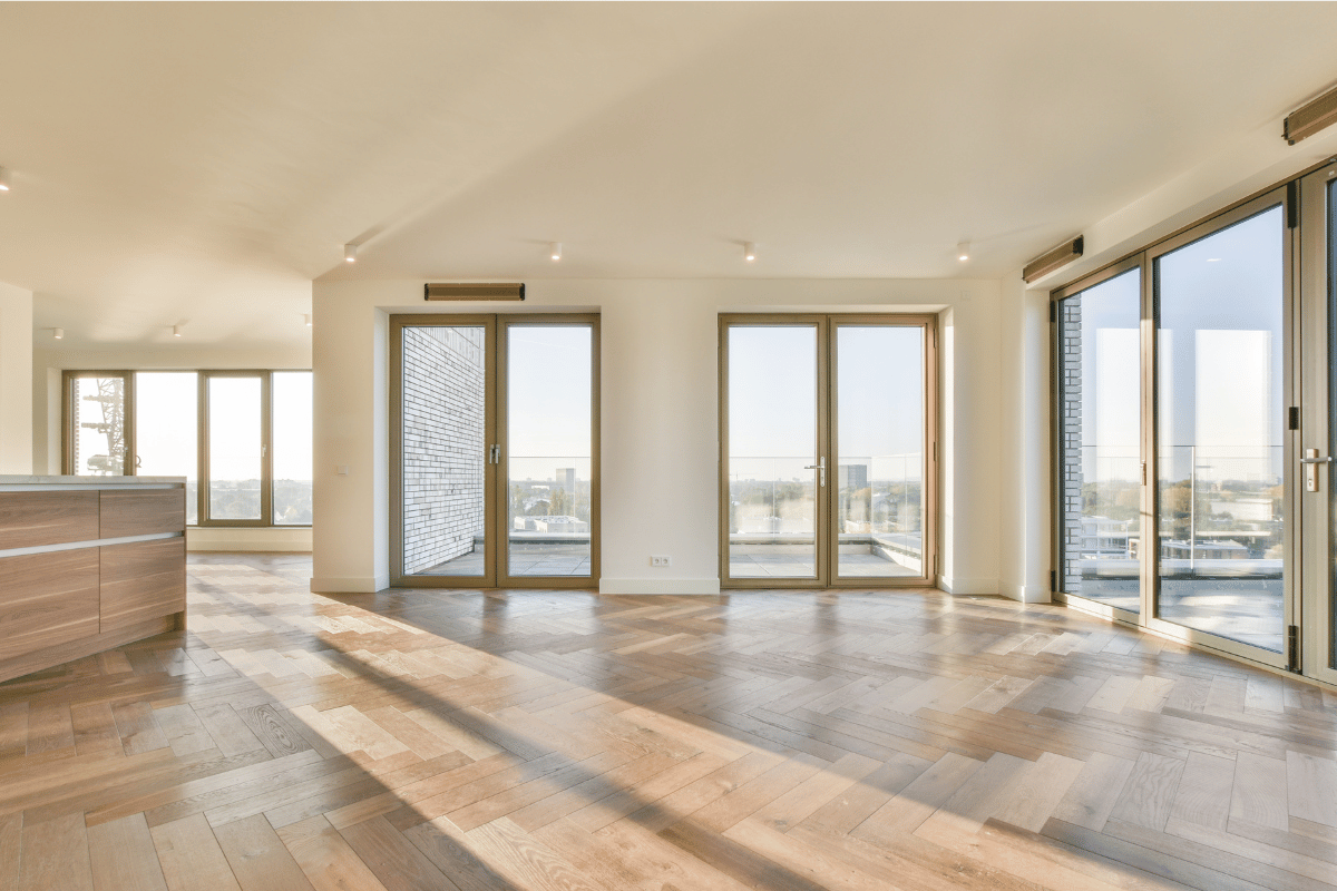 Bright empty modern apartment with large windows, wood floors, and city skyline views