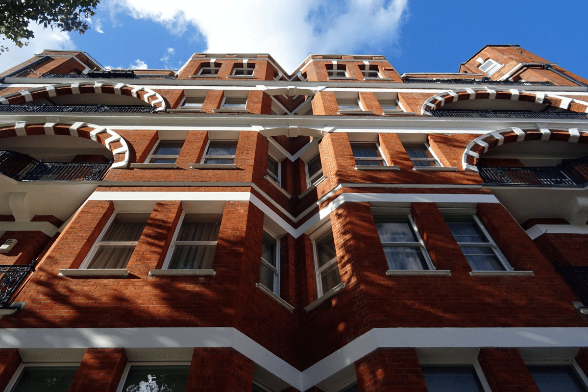 Low-angle view of a red-brick apartment building with white trim against a blue sky