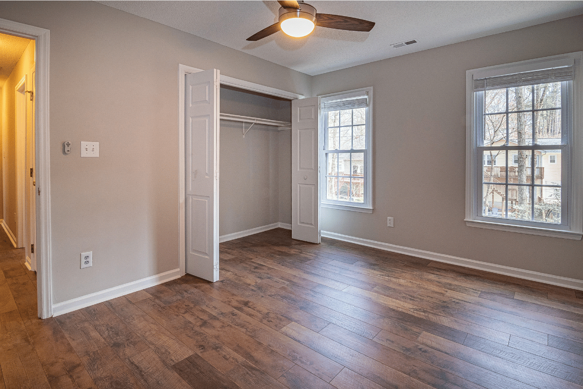 Empty bedroom with hardwood floors, beige walls, ceiling fan, and two windows