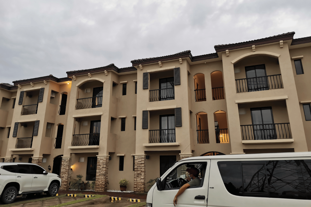 Three-story beige apartment building with balconies and parked white vans at dusk