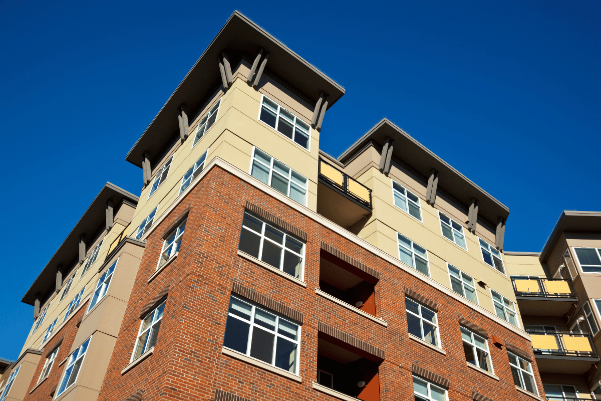 Low-angle view of a brick and beige apartment building against a clear blue sky