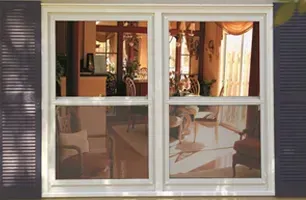 Living room seen through a white-framed window with sheer curtains and warm sunlight