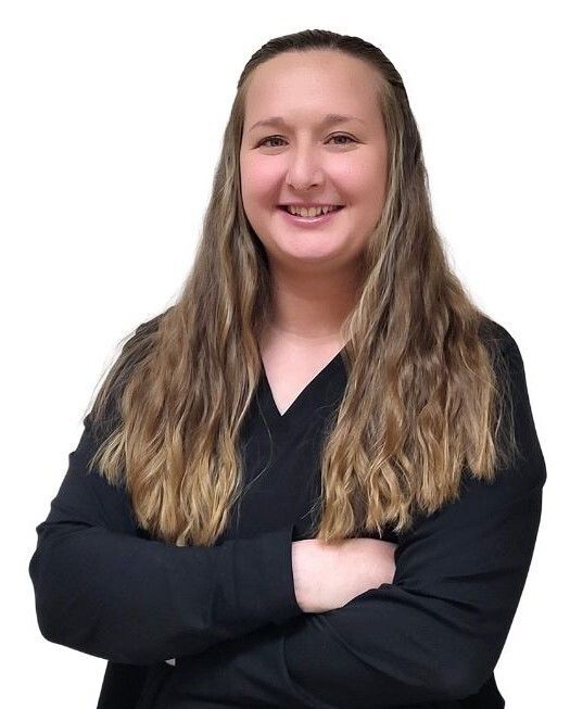 Woman with long hair, wearing a black shirt, smiles with arms crossed.