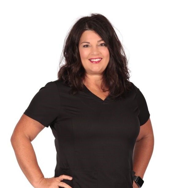 Woman with dark hair in black top smiles, hands on hips.