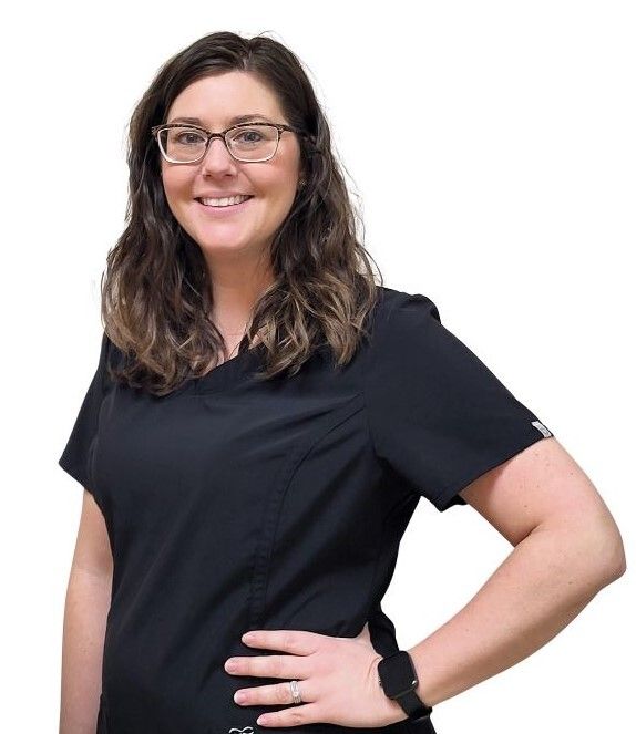 Woman in black scrubs smiles, wearing glasses, hand on hip.