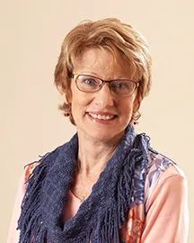 Woman wearing glasses and a blue scarf smiles at the camera.