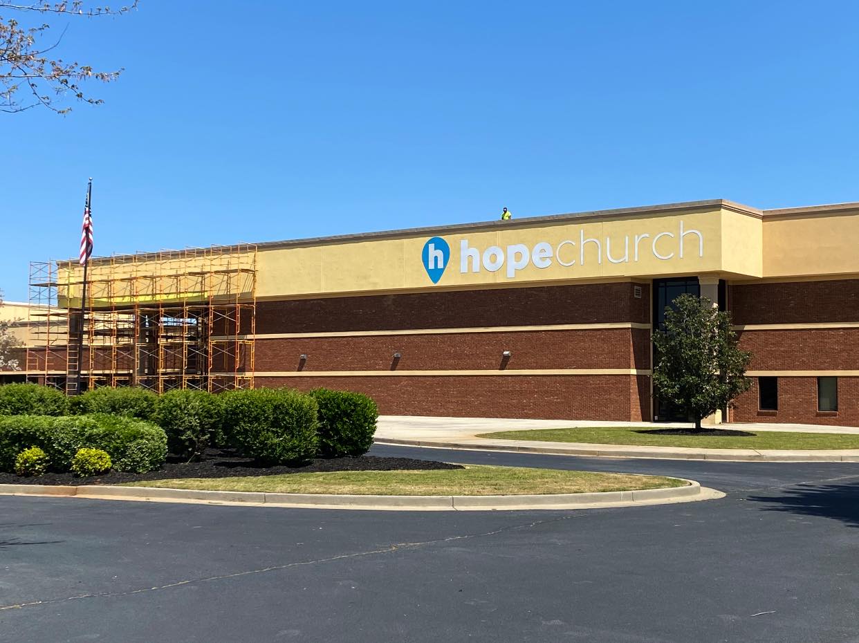 Hope Church building with brick and yellow exterior, American flag, blue sky.