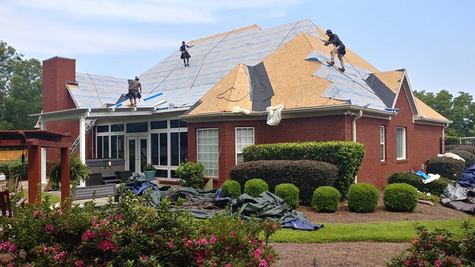 Roofers working on a red brick house, removing old shingles and preparing for new installation.