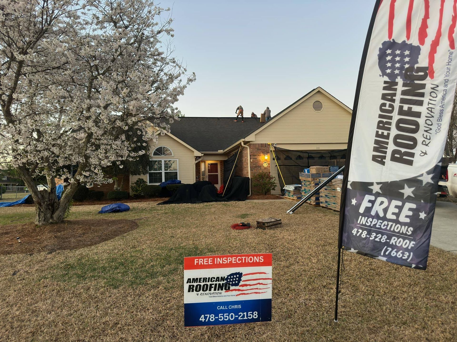 American Roofing and Renovation crew installing a residential shingle roof with company banners and yard signs visible