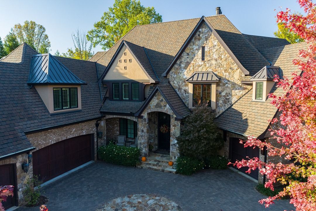 Stone and brown roofed house with a circular driveway and red garage doors.
