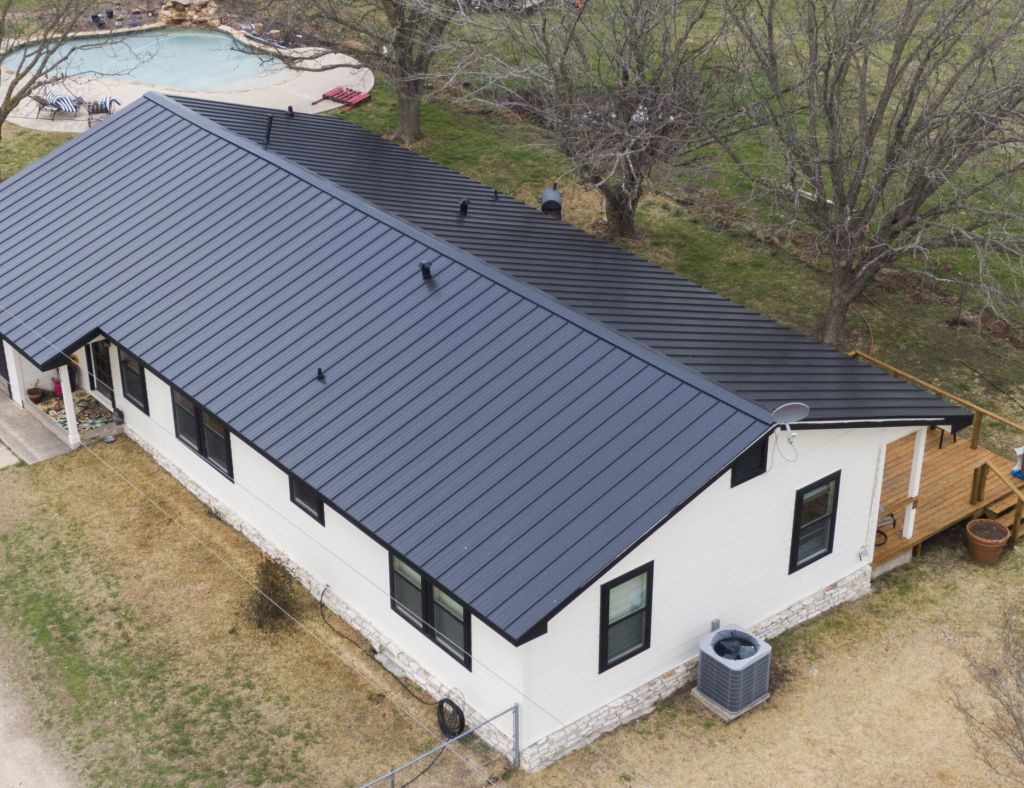 White house with a black metal roof, a deck, and a pool in the background.