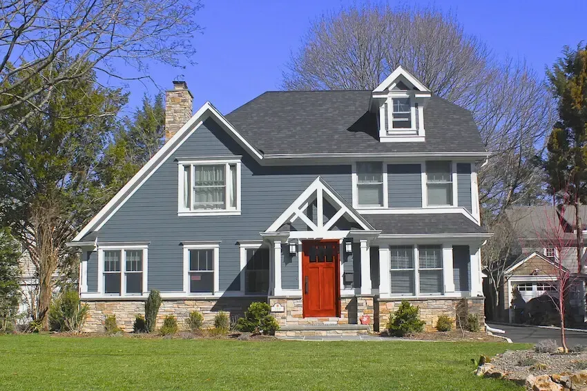 Blue and white house with red door, stone facade, and green lawn.