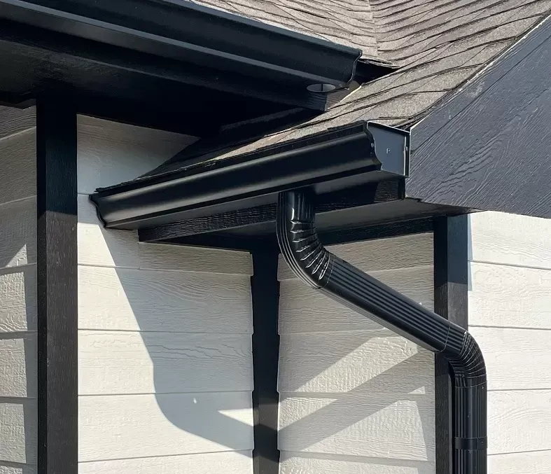 Black gutters on a house with white siding and a dark roof.