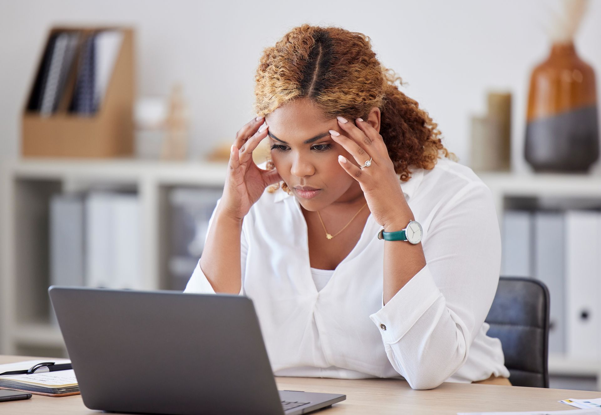 A woman is sitting at a desk looking at a laptop computer.