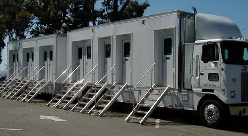 White mobile office trailer with multiple doors and metal stairs parked outdoors